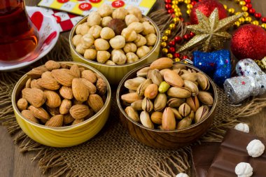 Beyaz ahşap yüzeyde bambu kaselerinde fındıklar, Noel süsü çay ve oyun kartları, yakın plan.