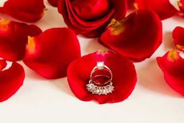 Beş taş elmas, beyaz yüzeyde taze gül yapraklı altın yüzükler. Kavramsal görüntü..