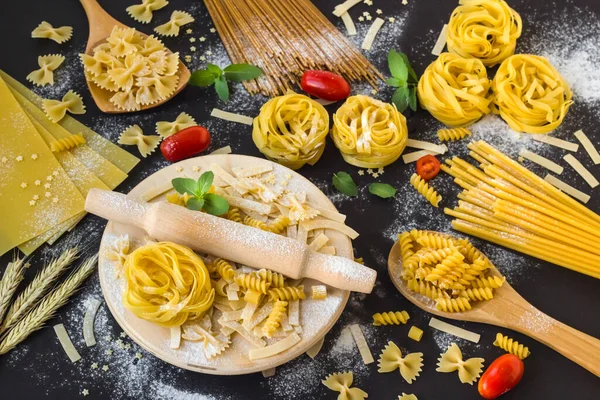 Types of pasta or macaroni on black surface with fresh mint and cherry tomatoes