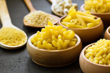 Pişmemiş makarna çeşitleri, siyah bir yüzey üzerindeki bambu kaselerinde dizayn edilmiş.