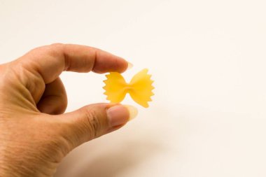 Bilinmeyen bir el beyaz bir yüzey üzerinde yay şeklinde ya da farfalle makarna tutuyor..