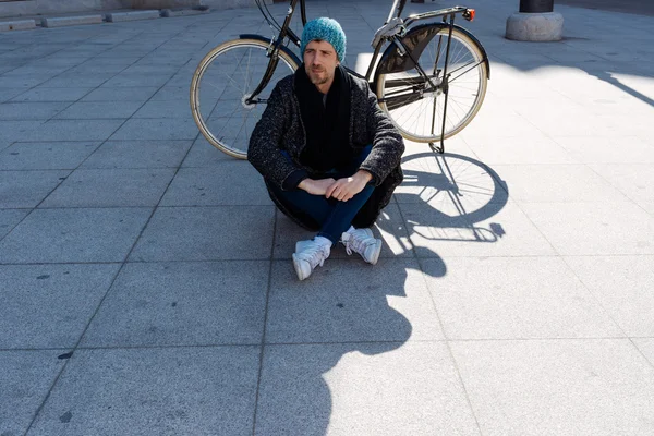 Homem sentado no chão com sua bicicleta na sombra — Fotografia de Stock