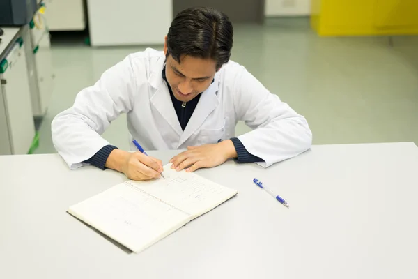 Investigador guapo escribiendo en su libro de laboratorio — Foto de Stock