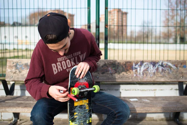 Man zit op een bankje terwijl de opbrengt van zijn Skate — Stockfoto