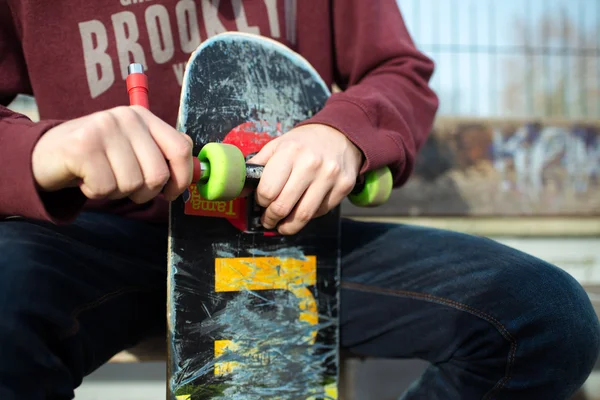 Close-up: Homem reparando seu skate em um banco na rua — Fotografia de Stock