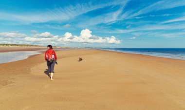 woman walking on a beach with a dog clipart