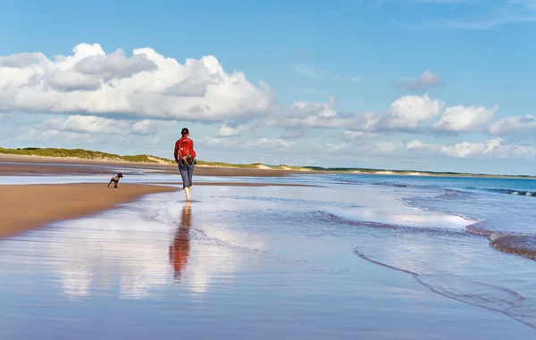 Donna che cammina su una spiaggia con un cane — Foto Stock