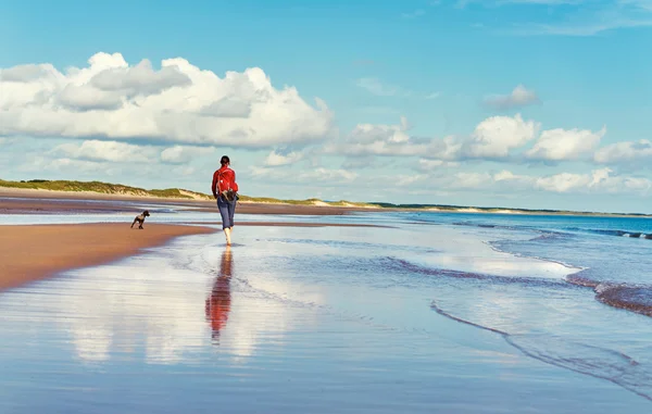 Γυναίκα που περπατά σε μια παραλία με ένα σκυλί — Φωτογραφία Αρχείου