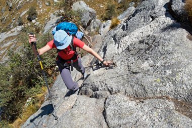 Female hiker climbing up on rock clipart