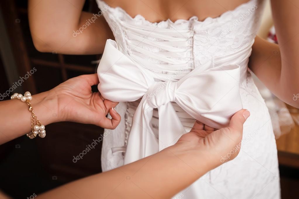 Bridesmaid helps to bride to put on wedding dress.