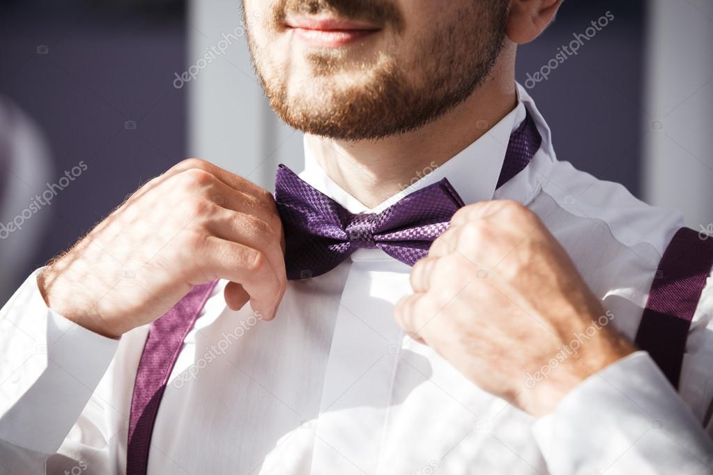 Groom puts on violet bow tie.