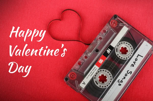 Tarjeta de San Valentín. Cassette de audio vintage con cinta suelta dando forma a un corazón sobre fondo rojo —  Fotos de Stock