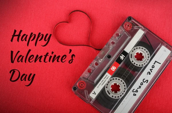 Tarjeta de San Valentín. Cassette de audio vintage con cinta suelta dando forma a un corazón sobre fondo rojo —  Fotos de Stock