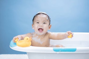 Bebeğin küvette banyo yapması ve mavi arka planda sarı ördekle oynaması.