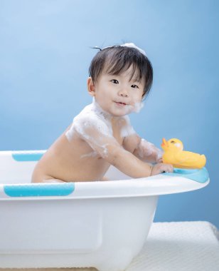 Bebeğin küvette banyo yapması ve mavi arka planda sarı ördekle oynaması.