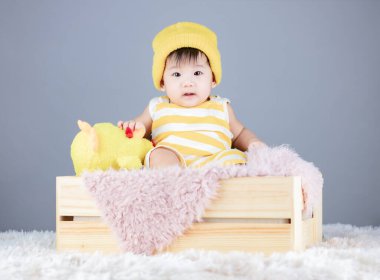 Bib Pantalonlu şirin bebek. Kıyafet takımı. Şapka sarısı olan çocuk tahta kutuda yatıyor.