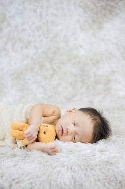 Küçük bebek uzanmış oyuncak ayıya sarılıyor.