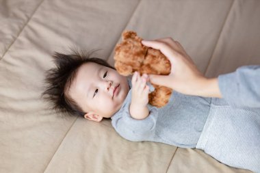 Bebek, El 'e bakıyor Oyuncak ayıyı bebeğin üstünde tutuyor.