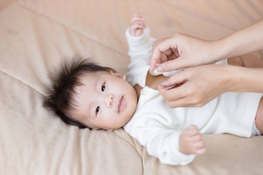 Anne bebeğine elbise giydiriyor.