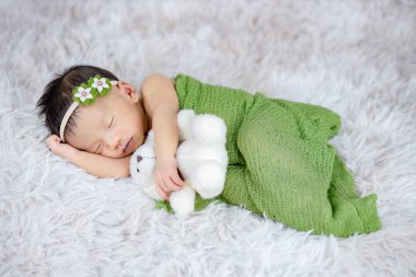 Küçük bebek uzanmış oyuncak ayıya sarılıyor