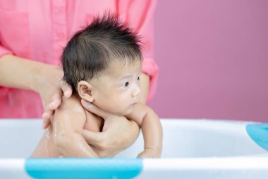 Yenidoğan, annesinin pembe arka planında havuzda banyo yapıyor.