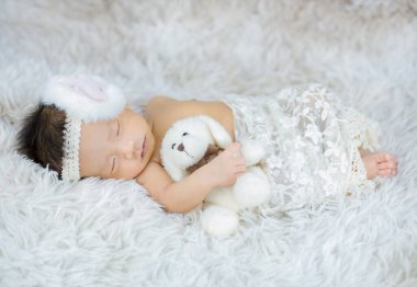 Küçük bebek uzanmış oyuncak ayıya sarılıyor.