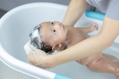 Bebek banyo yapıyor, anne elleri başını destekliyor..