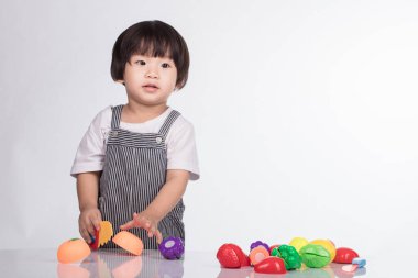 Beyaz arka planda izole edilmiş oyuncak bıçakla sebze ve meyve kesen çocuk.