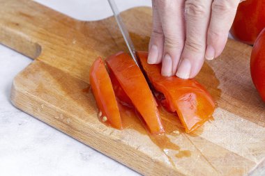 Tanınmayan kadın elleri tahta bir tahtada taze domates dilimleri kesiyor.