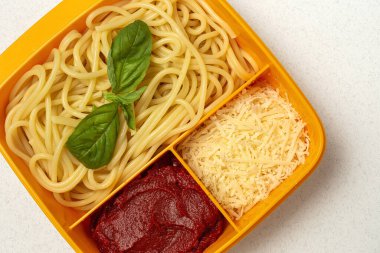Plastik kutulardaki sağlıklı yiyecekler, çalışma masasında ev yapımı spagetti, domates, peynir ve fesleğen ile birlikte yemeye hazır. İtalyan yemeği. Götürmek için.