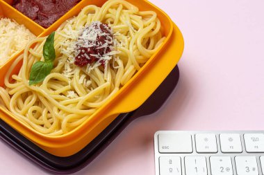 Plastik kutulardaki sağlıklı yiyecekler, çalışma masasında ev yapımı spagetti, domates, peynir ve fesleğen ile birlikte yemeye hazır. İtalyan yemeği. Götürmek için.