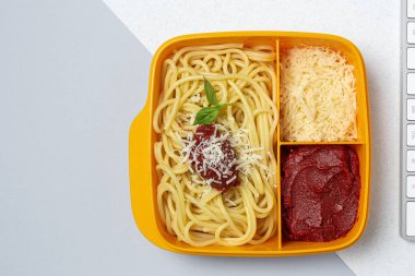 Plastik kutulardaki sağlıklı yiyecekler, çalışma masasında ev yapımı spagetti, domates, peynir ve fesleğen ile birlikte yemeye hazır. İtalyan yemeği. Götürmek için.