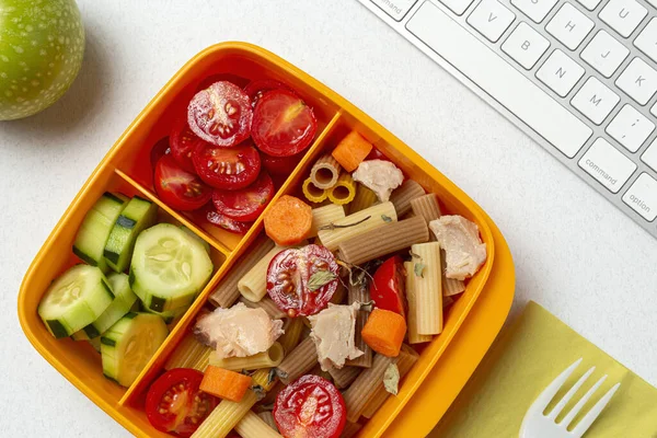 Lunch at work place healthy pasta with tuna, cherry tomatoes, carrot, cucumber in lunch box on work table. Home food for office concept