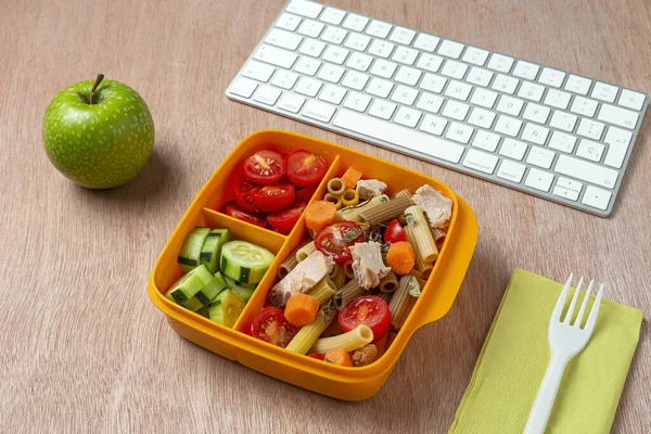 Lunch at work place healthy pasta with tuna, cherry tomatoes, carrot, cucumber in lunch box on work table. Home food for office concept