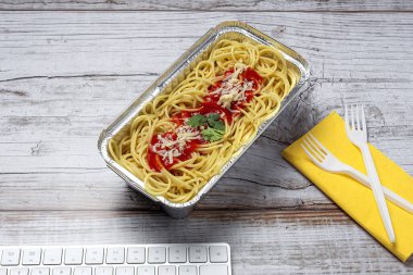 İş yerinde öğle yemeği ve bilgisayar klavyeli domates ve peynirli sağlıklı spagetti. Ofis konsepti için ev yemeği. Yemeği götür.