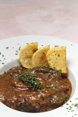 Ev yapımı Osso Buco eti aromatik bitki sosu, kırmızı şarap ve patates kızartması.