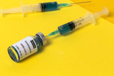 COVID-19 aşısı olan şeffaf cam şişeler, renkli arka planda şırıngalar. Seçili odak.