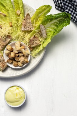 Romanin, peynir, kızarmış ekmek, tavuk, limon ve soslu ev yapımı Sezar Salatası. Beyaz ahşap arka planda
