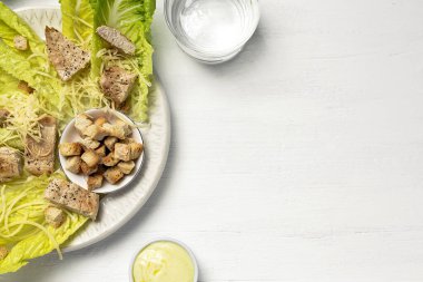 Romanin, peynir, kızarmış ekmek, tavuk, limon ve soslu ev yapımı Sezar Salatası. Beyaz ahşap arka planda