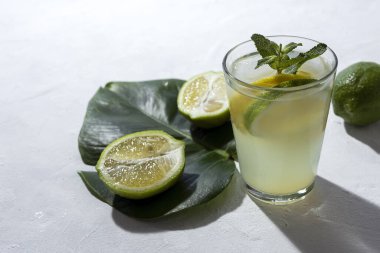 Buzlu ev yapımı cam limonata ve beyaz arka planda gün ışığında nane şekeri.