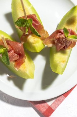 Dilimlenmiş taze kavun jambonlu ve renkli arka planda güneş ışığı var. İspanyol gıda konsepti