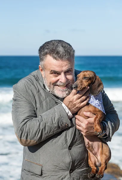 Homem barbudo atraente na praia Com cão dachshund vermelho — Fotografia de Stock