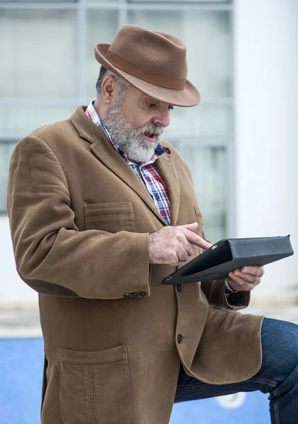 Vieil homme attrayant avec barbe et chapeau avec une tablette — Photo