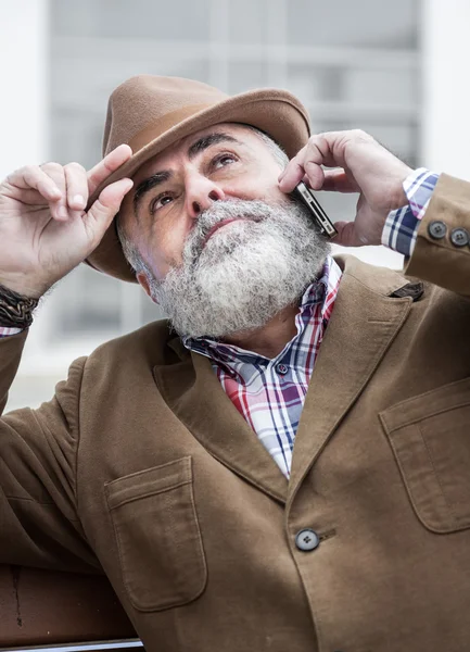 Velho atraente com barba e chapéu falando ao telefone — Fotografia de Stock