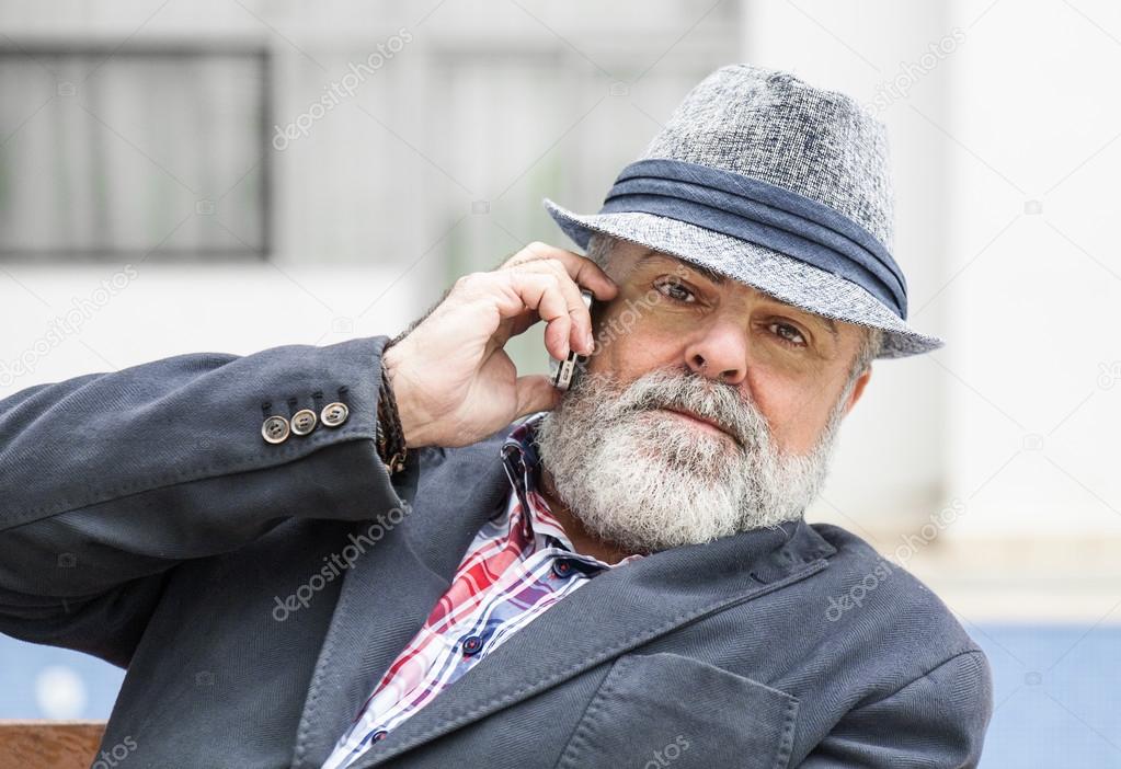 Attractive old man with beard and hat talking on phone