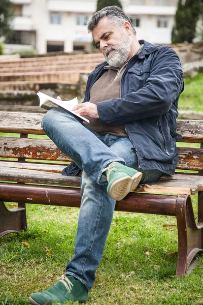Homem barbudo atraente lendo em um parque — Fotografia de Stock