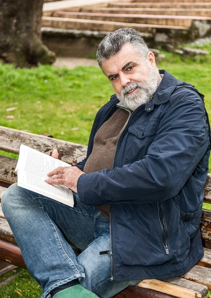 Homem barbudo atraente lendo em um parque — Fotografia de Stock