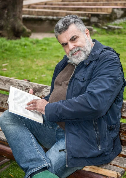 Homem barbudo atraente lendo em um parque — Fotografia de Stock