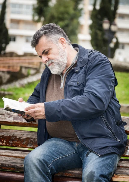 Homem barbudo atraente lendo em um parque — Fotografia de Stock