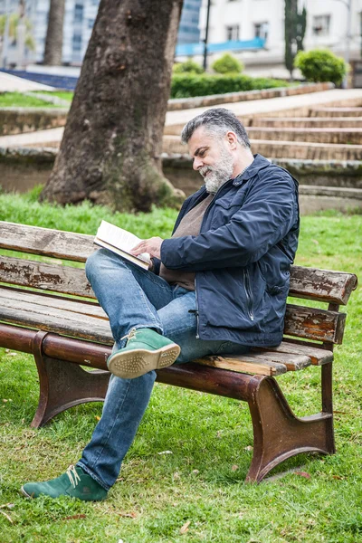 Homem barbudo atraente lendo em um parque — Fotografia de Stock